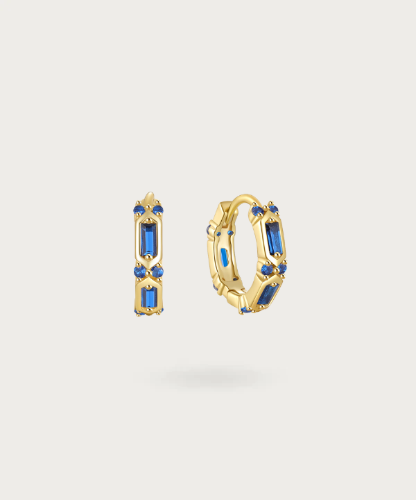Step into luxury with Lluminada's hoops, capturing the brilliance of fiery red or deep blue zirconia set in a gold backdrop.