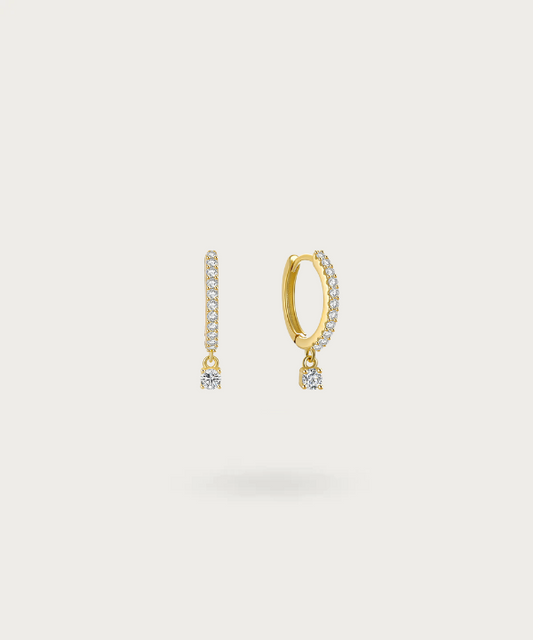 Sol's silver hoop earrings studded with shimmering zirconias and a dangling charm.