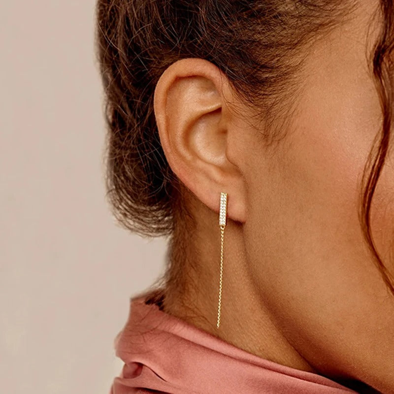 "Elegantly descending zirconia in Gina's long golden earrings create a captivating display."